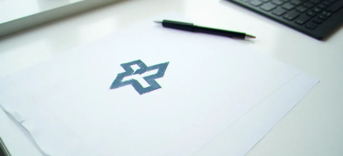 Vue plongeante sur un bureau épuré avec un croquis de logo en bleu foncé sur papier blanc, illustrant la création d'un business France logo en contexte professionnel